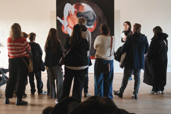 Groep mensen bekijkt een abstract schilderij met warme kleuren in een helder verlichte galerijruimte.
