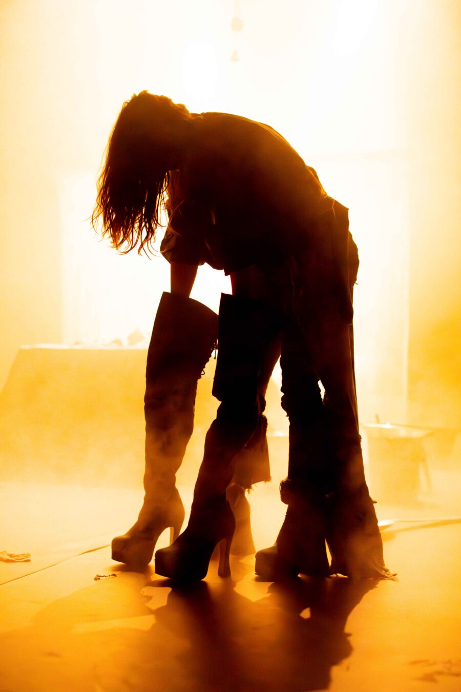 silhouet van een vrouw die voorovergebogen staat met haar handen in een paar grote laarzen. silhouette of a woman bent forwards, with her hands in a pair of huge boots.
