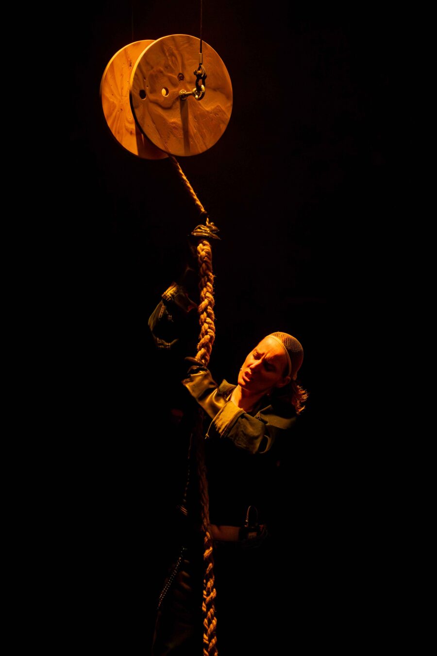 vrouw trekt aan een dikke koord, die aan een katrol hangt die in de lucht hangt. woman pulling a thick cord hanging from a pulley that is hanging in the air.